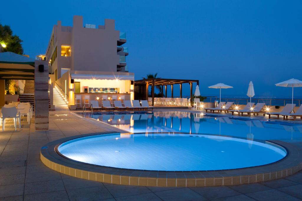 a swimming pool at night with chairs and umbrellas at Erytha Hotel & Resort Chios in Karfas