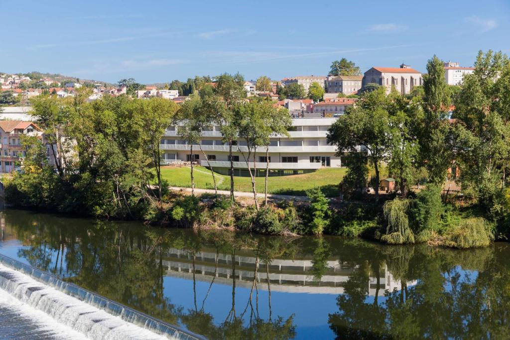 a building next to a river with trees at Best Western Plus Hotel Divona Cahors in Cahors