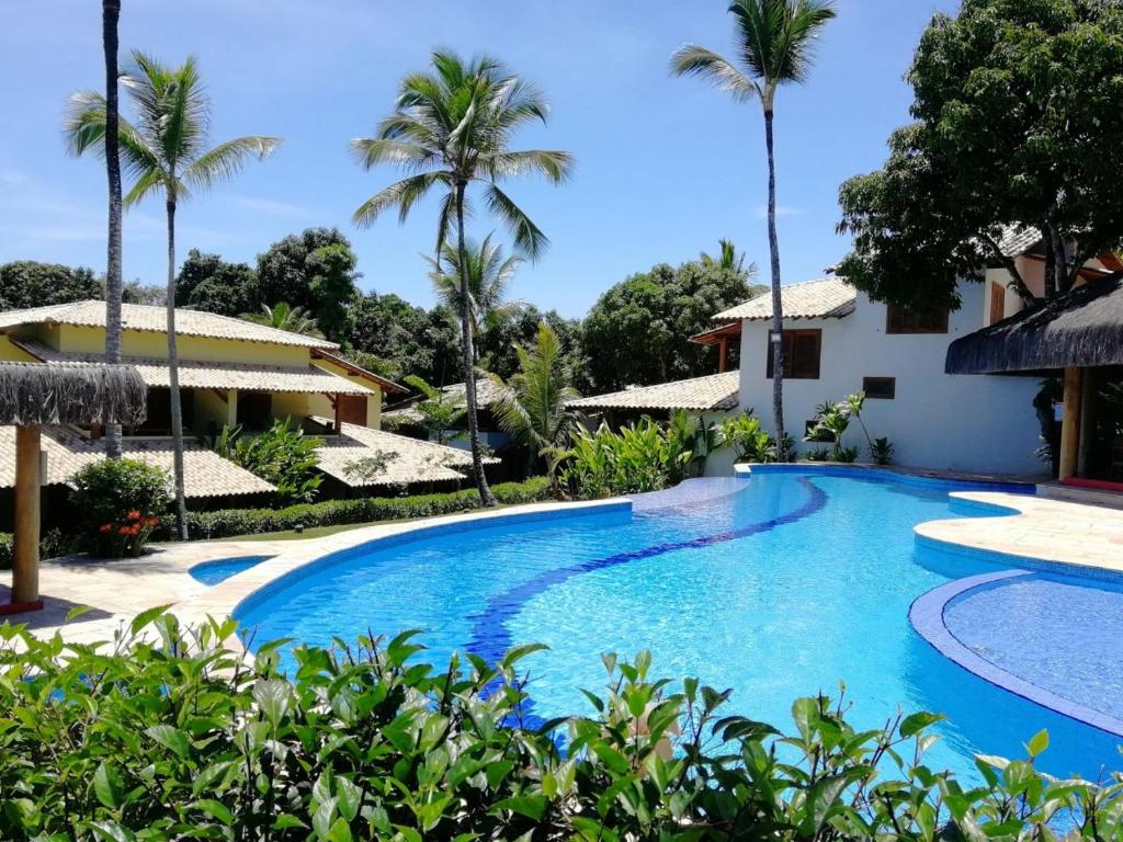 a swimming pool in front of a house with palm trees at Charm Bahia Residencias in Arraial d'Ajuda