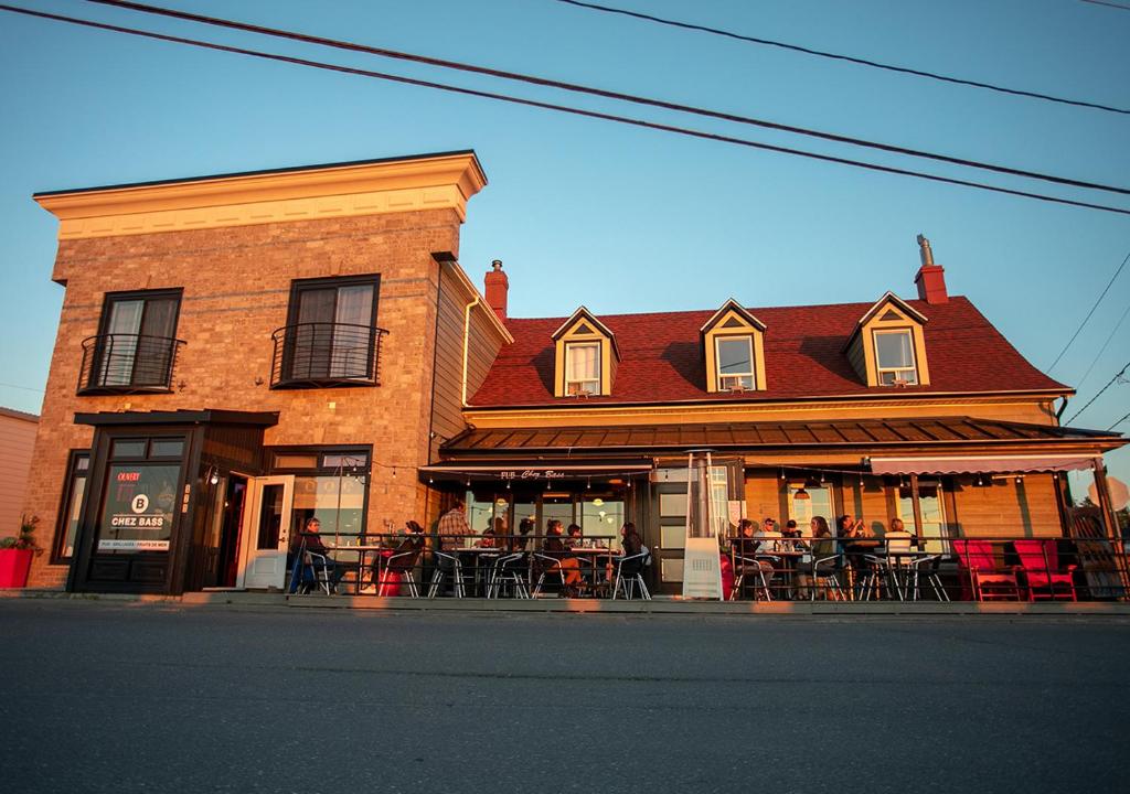 a brick building with tables and chairs on a street at Le Littoral Bistro Gourmand et Auberge in Sainte-Anne-des-Monts