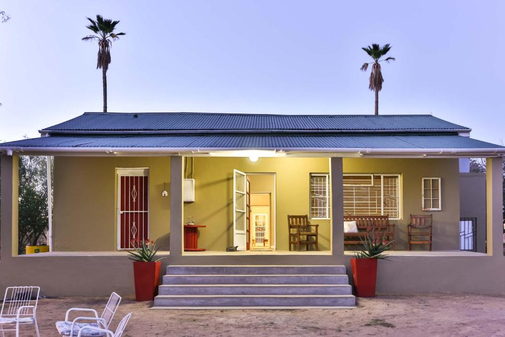 ein kleines gelbes Haus mit zwei Palmen in der Unterkunft Hazenjacht Karoo Lifestyle - Oom Manus se Huis in Oudtshoorn