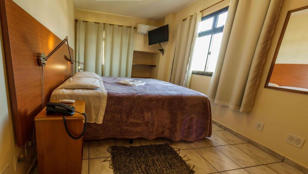 a bedroom with a bed and a phone on a table at Hotel Vila Rica Flat in Resende