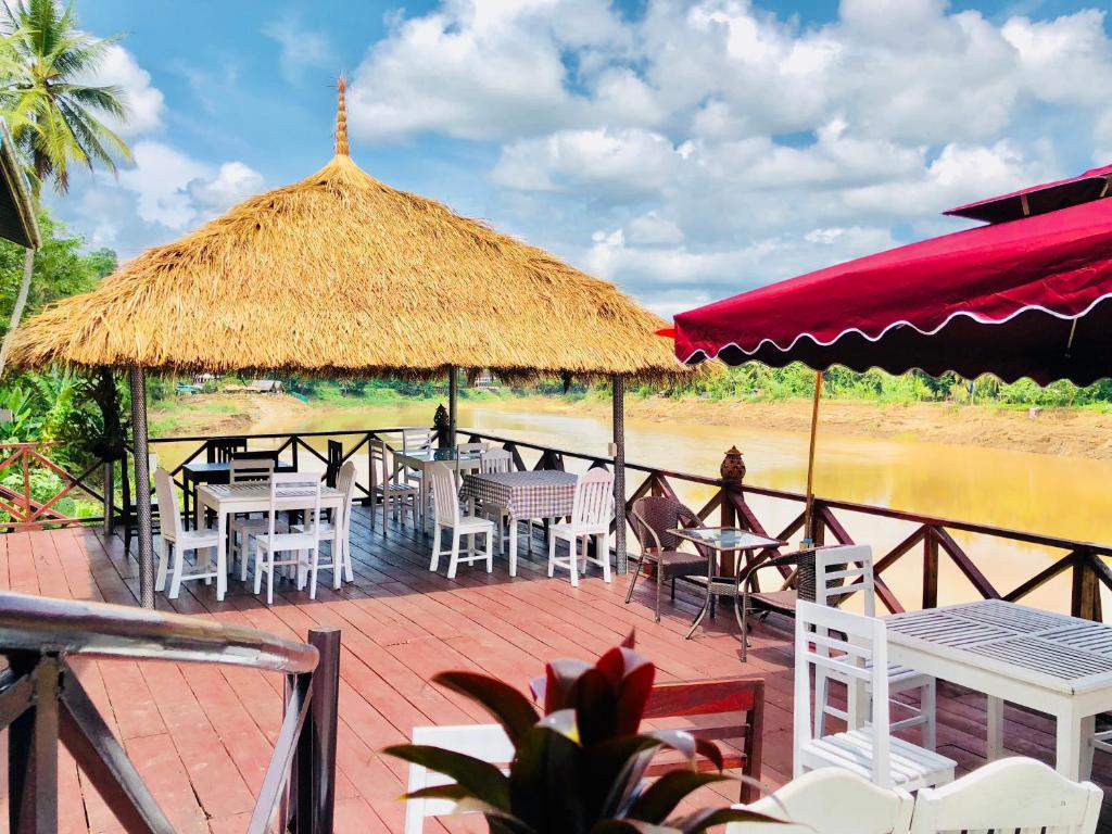 a deck with tables and chairs and a straw umbrella at Merry Riverside Hotel in Luang Prabang