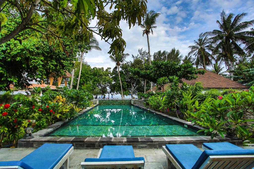 a swimming pool in a garden with two blue chairs at Blue Marlin Air in Gili Islands
