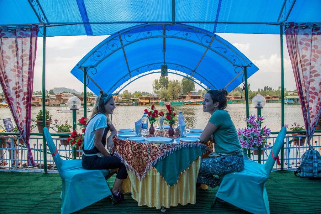 dos mujeres sentadas en una mesa bajo una carpa azul en Swan Group of Houseboats, Golden Dal Lake, en Srinagar