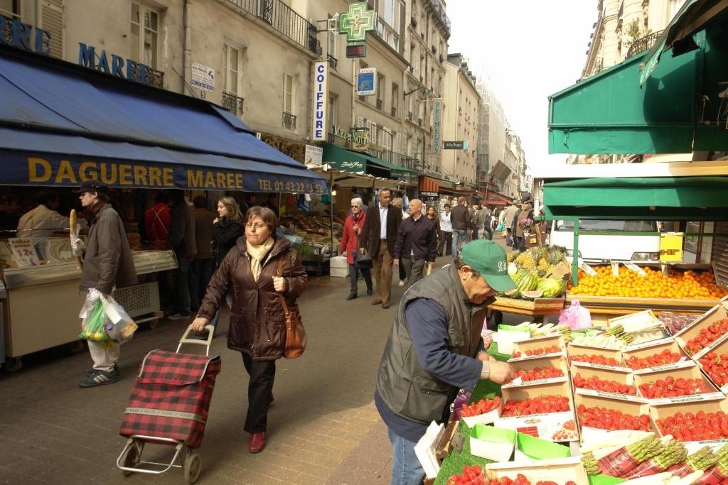 un grupo de personas caminando por un mercado con frutas y hortalizas en Montparnasse Daguerre en París