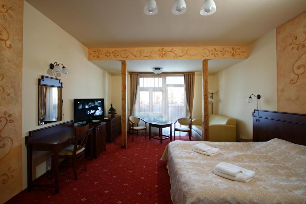 Sunlit deluxe room with neatly folded towels on bed, desk, TV, and window seating area.