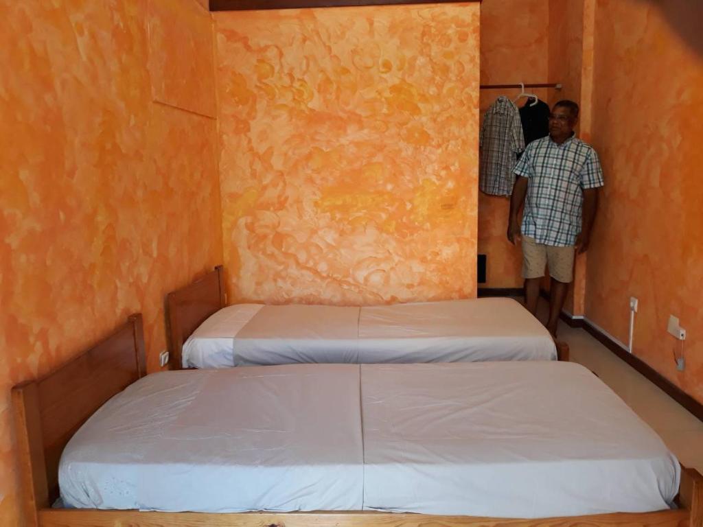 a man standing in a room with two beds at Turtle Hostel - Private Room - City Center in Sal Rei