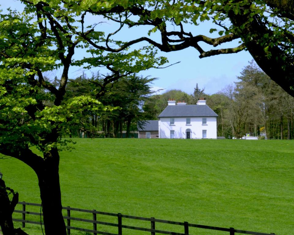 a white house on a green field with a fence at Cannaway House B&B in Macroom