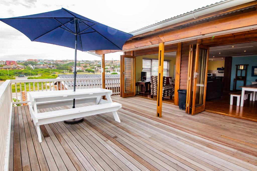 a bench on a deck with an umbrella at Happy Waves Holiday Home in Jeffreys Bay