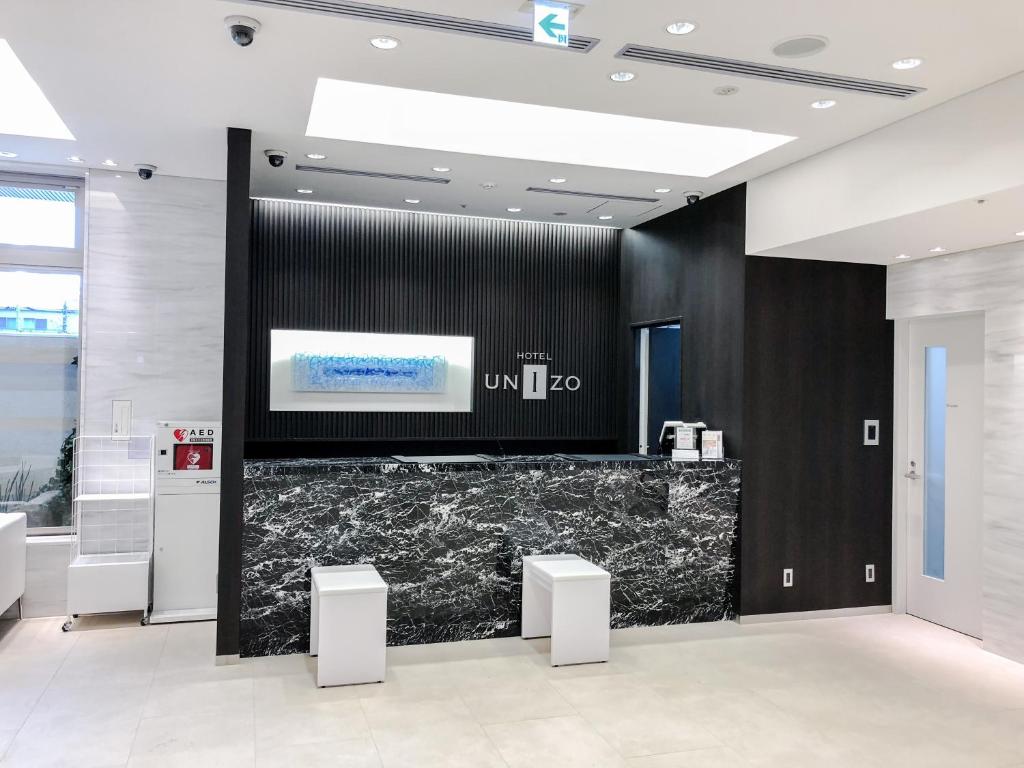 a lobby with a black wall and a counter with stools at HOTEL UNIZO Yokohamaeki-West in Yokohama