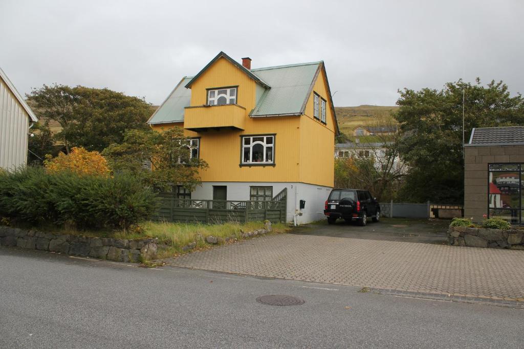 una casa amarilla con un coche aparcado delante de ella en Cosy Guesthouse anno 1936, en Sandavágur