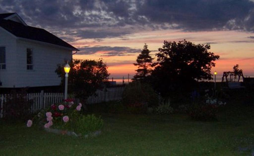 a sunset in a yard with a house and flowers at Gite La Ptite Falaise hébergement touristique in Sainte-Anne-des-Monts