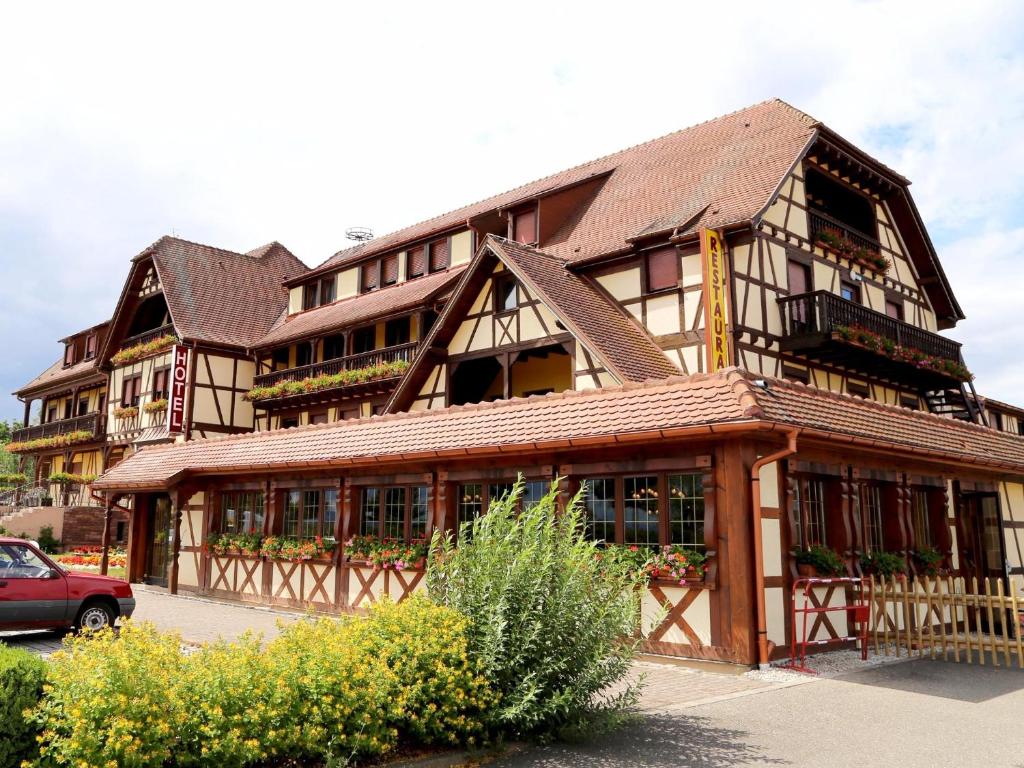 un grande edificio in legno con un'auto parcheggiata di fronte di Hotel Au Parc des Cigognes a Kintzheim