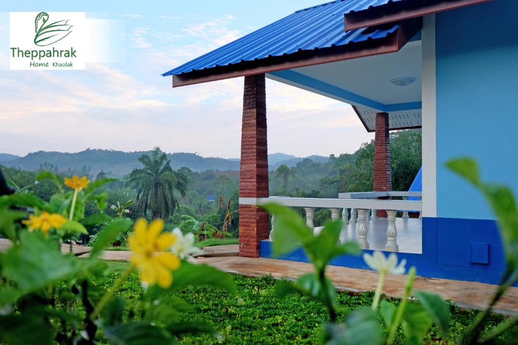 a building with a blue roof with flowers in the foreground at Theppahrak Home Khaolak in Khao Lak