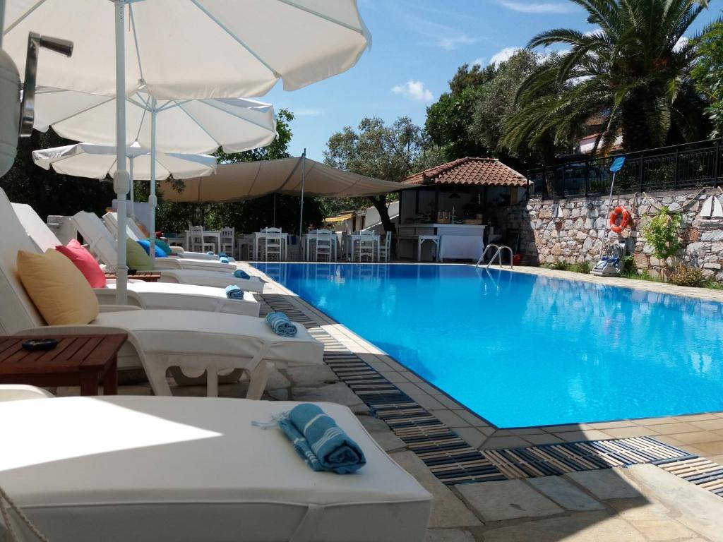 a swimming pool with white chairs and umbrellas at Anofli Suites in Skopelos Town