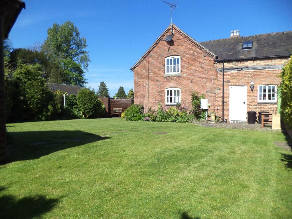 une maison en briques avec une grande pelouse devant elle dans l'établissement Lapwing Cottage, à Stoke-on-Trent