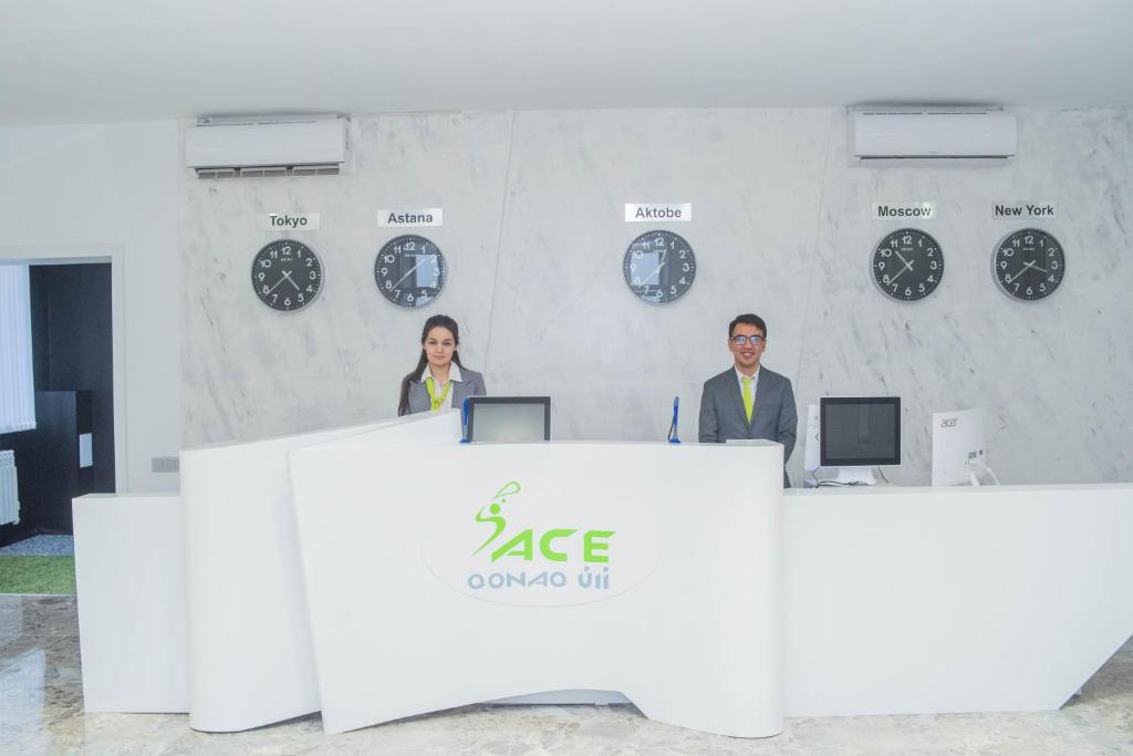 two people standing behind a desk with clocks on the wall at Aсe Hotel in Aktobe