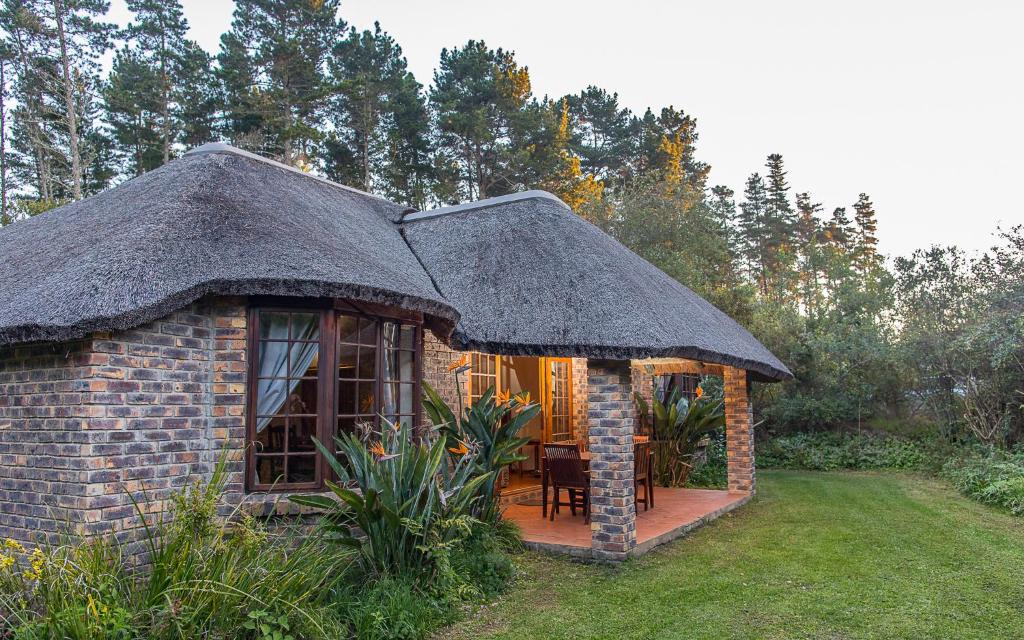 una pequeña casa de ladrillo con techo de paja en Coral Tree Cottages, en Harkerville