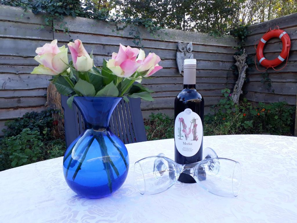 a blue vase with pink roses and a bottle of wine at Private Logies Texel Woodart in Midden-Eierland