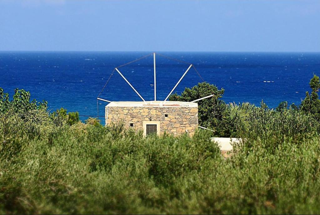 a building on a hill with the ocean in the background at Authentic Cretan Stone Windmill in Sitia