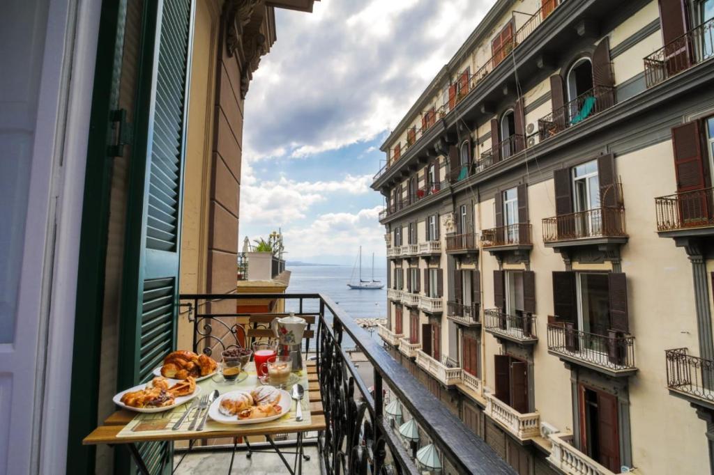 einen Balkon mit einem Tisch und Blick auf das Wasser in der Unterkunft Di Palma Suite in Neapel
