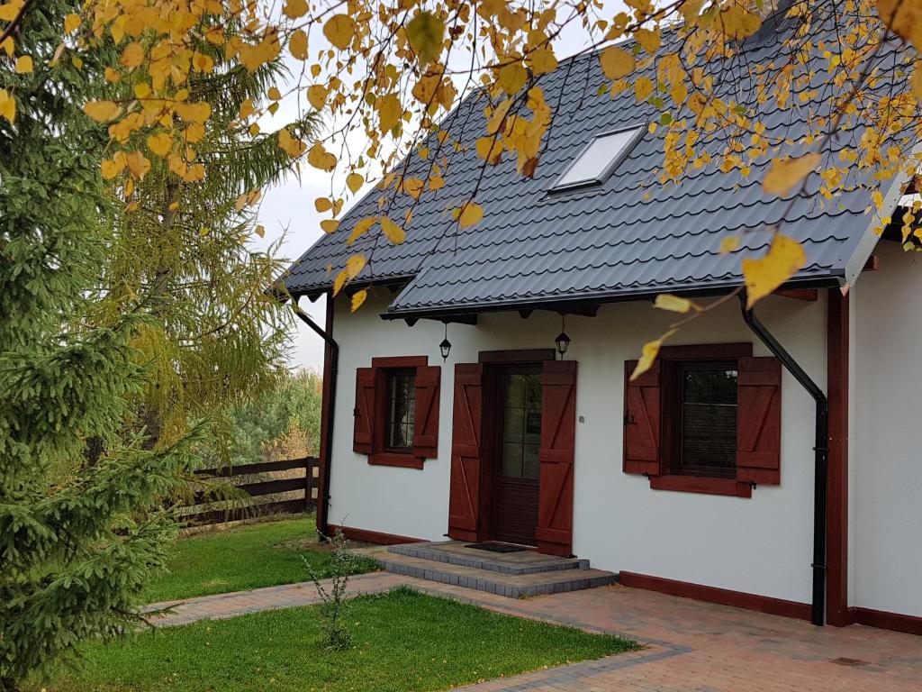 a small white house with red windows and a roof at 4 Pory Kaszub - Domek z banią i sauną in Skoszewo