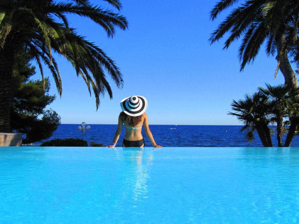 a woman in a hat standing in a swimming pool looking at the ocean at La Villa Mauresque in Saint-Raphaël