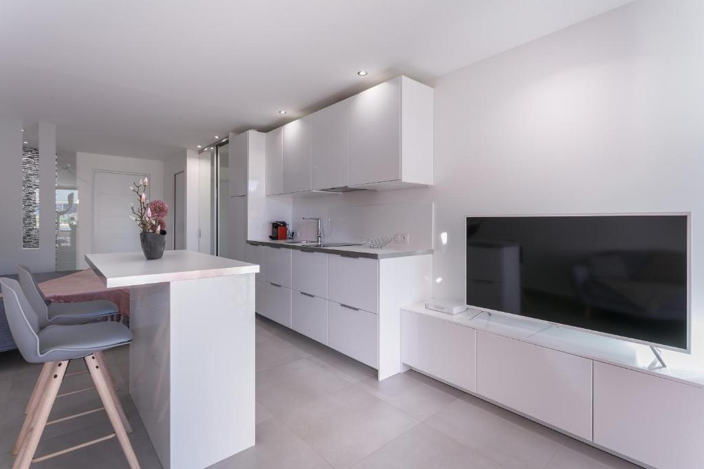 Il comprend une cuisine avec des placards blancs, une chaise et une télévision. dans l'établissement Cap d'Agde Naturiste, au Cap d'Agde