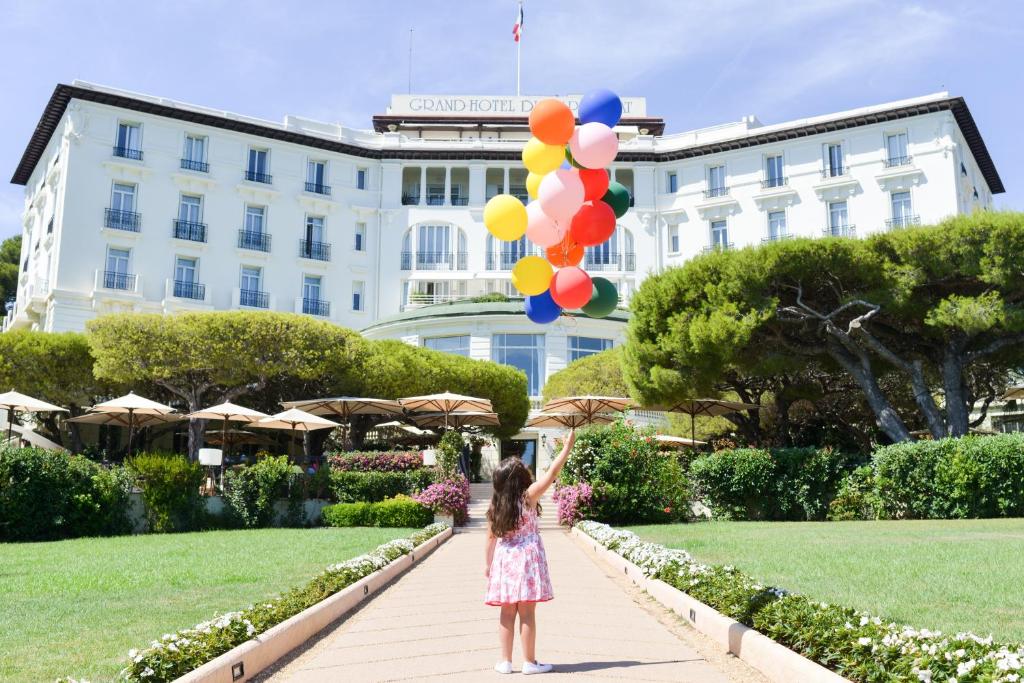a little girl holding balloons in front of a building at Grand-Hôtel du Cap-Ferrat, A Four Seasons Hotel in Saint-Jean-Cap-Ferrat
