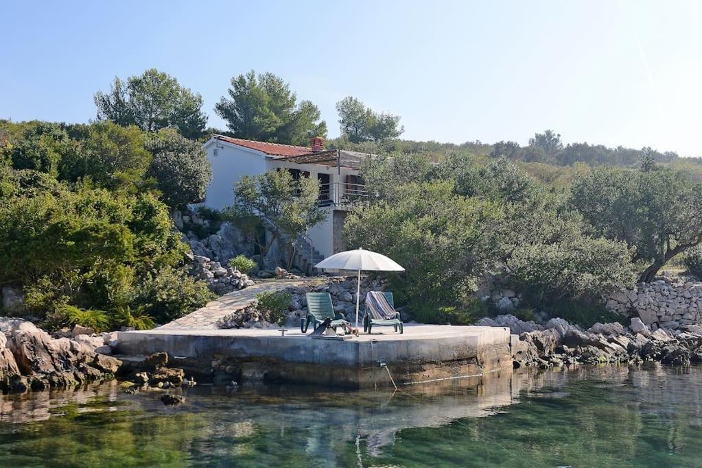 uma casa com um guarda-chuva e uma cadeira numa doca na água em Private island Šćitna - HOUSE LUEL em Murter