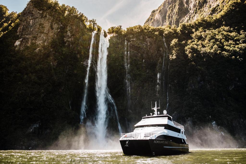 a boat in the water in front of a waterfall at Milford Sound Overnight Cruise - Fiordland Discovery in Milford Sound