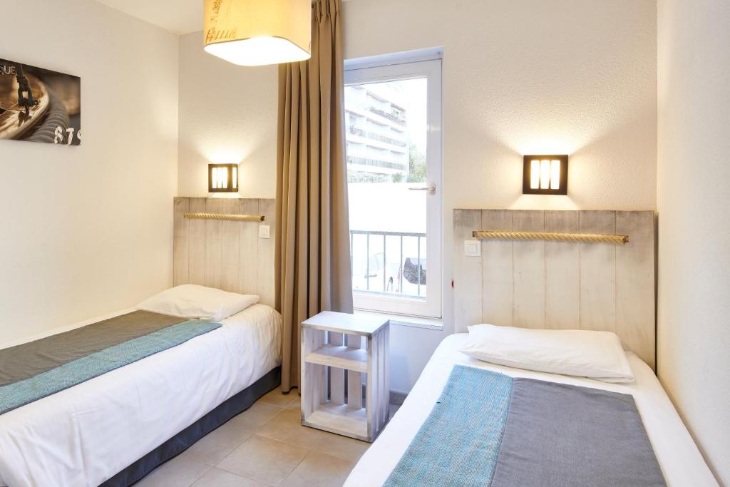 two beds in a small room with a window at Résidence Vacances Bleues Les Jardins d'Arvor in Bénodet