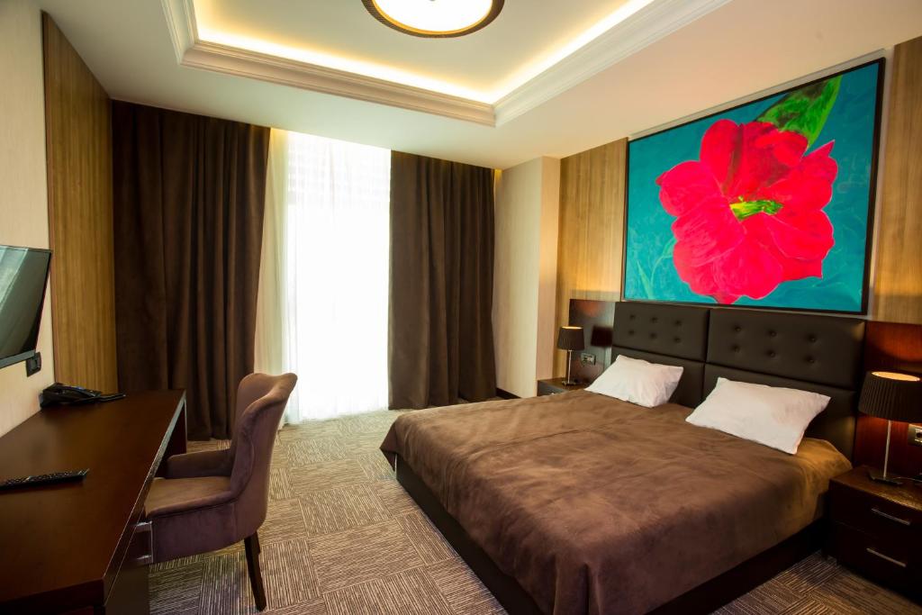 1 dormitorio con 1 cama, escritorio y un cuadro de flores rojas en AZPETROL HOTEL QUSAR, en Qusar