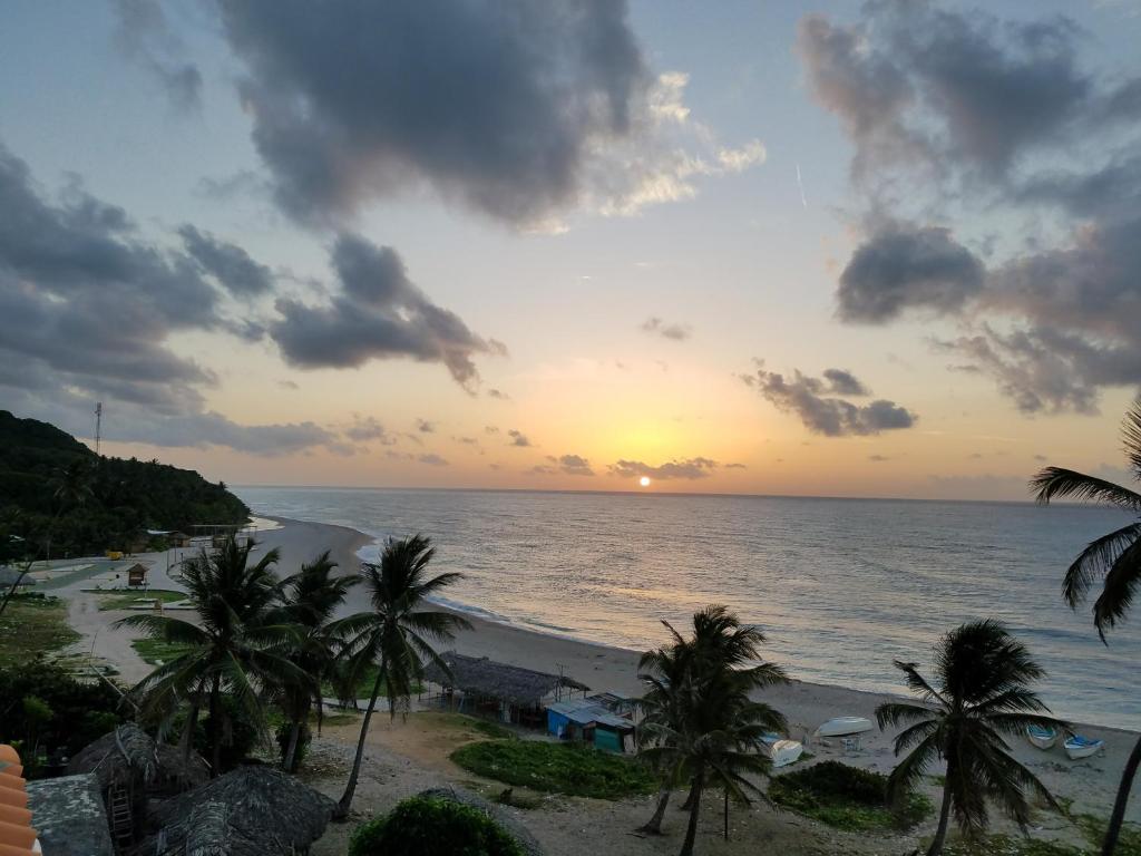 una puesta de sol sobre una playa con palmeras y el océano en Hotel Vista Sur, en Los Patos