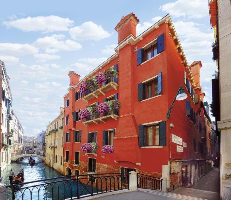 a red building with flower boxes on a canal at Hotel Mercurio in Venice