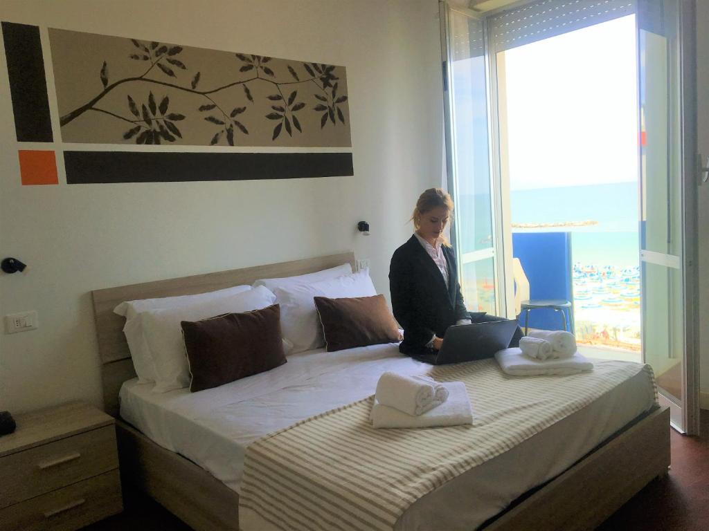una mujer está sentada en una cama con un portátil en Hotel al Nuovo Porto, en Bellaria-Igea Marina