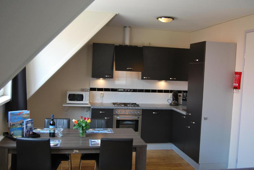 una cocina con mesa y una cocina con armarios negros en Wijnberg Appartementen en Hollum