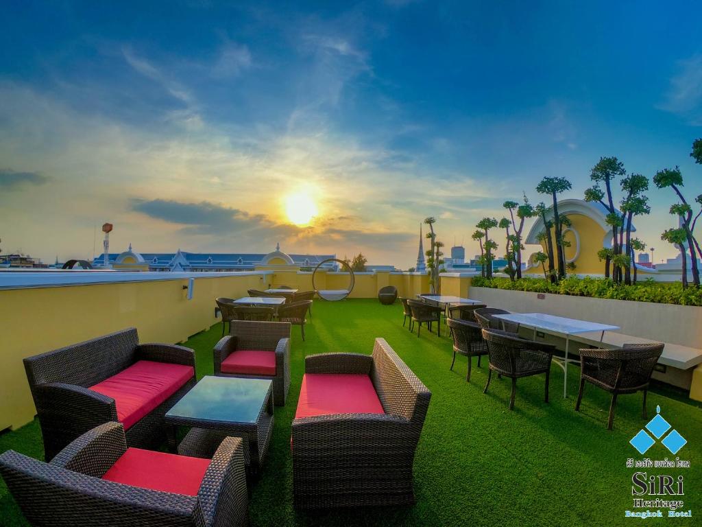 een patio met tafels en stoelen en de zonsondergang op de achtergrond bij Siri Heritage Bangkok Hotel - SHA Extra Plus in Bangkok