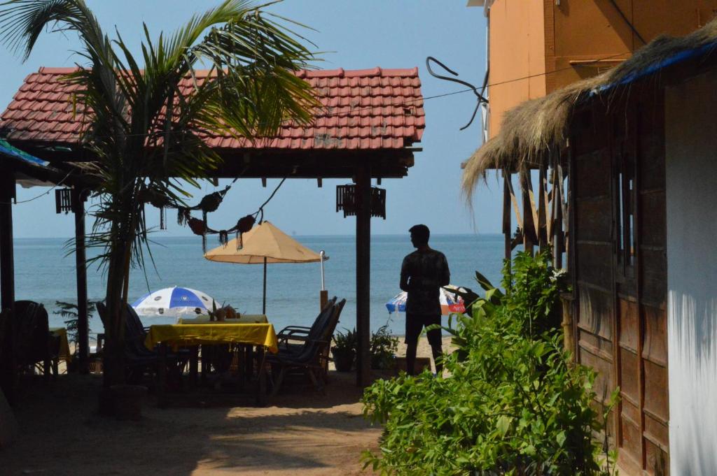 a man standing next to a table with the ocean at Soulmate Beach Resort in Agonda
