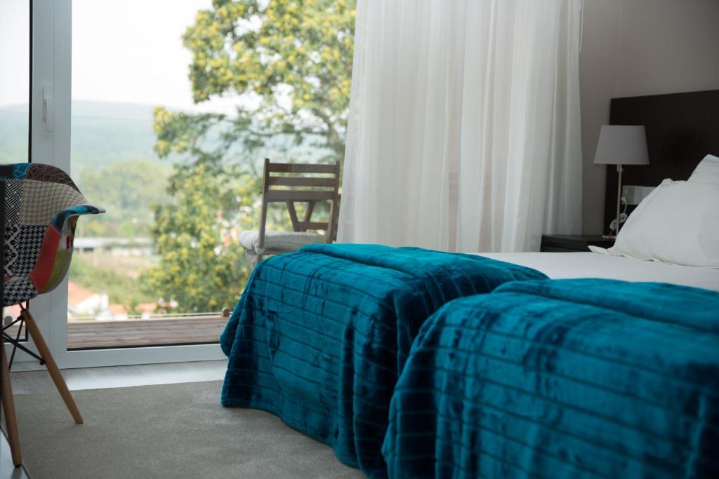 sypialnia z łóżkiem z niebieskim kocem i oknem w obiekcie Casa de Campo Memórias da Comarca w mieście Arganil