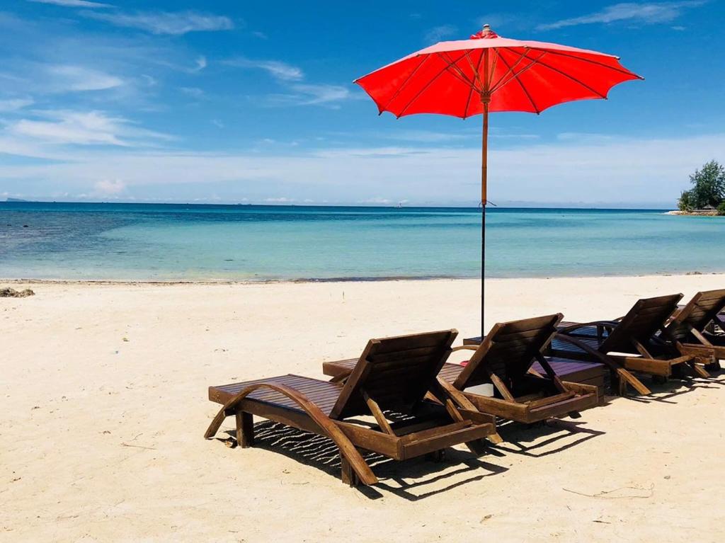 eine Gruppe von Stühlen und einem Sonnenschirm am Strand in der Unterkunft Phangan Cove Beach Resort in Srithanu