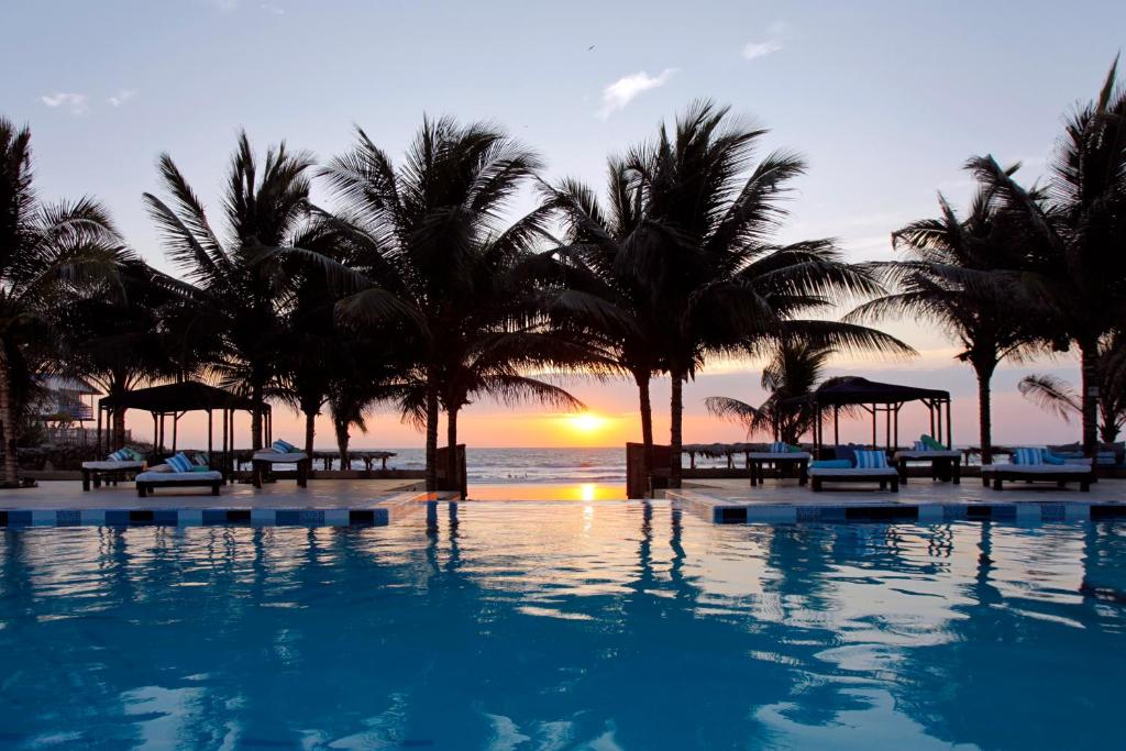 una piscina con palmeras y el océano al atardecer en Palmazul Hotel & Spa en San Clemente