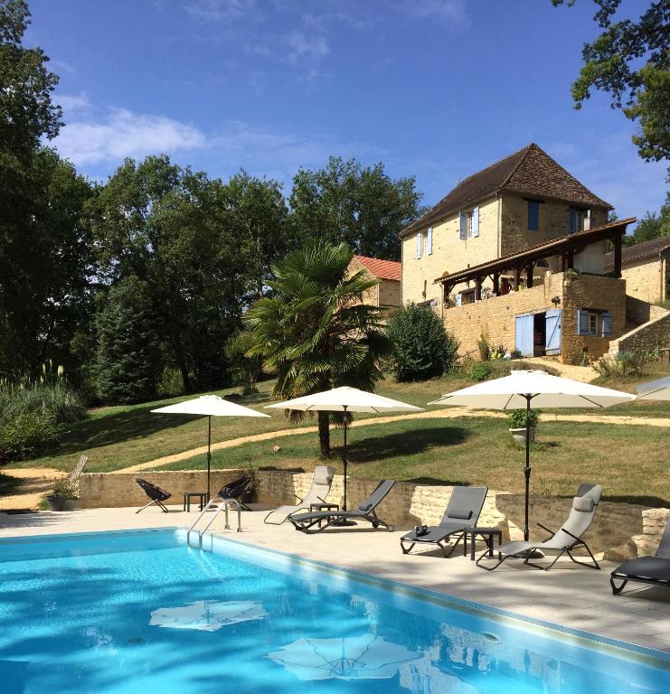 une piscine avec chaises et parasols devant une maison dans l'établissement Chambres d'hôtes Au Coeur De Lolhm, au Buisson de Cadouin