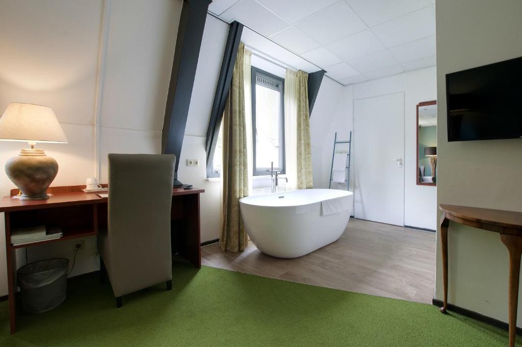 een badkamer met een bad, een bureau en een televisie bij Boetiek Hotel BonAparte Lochem in Barchem