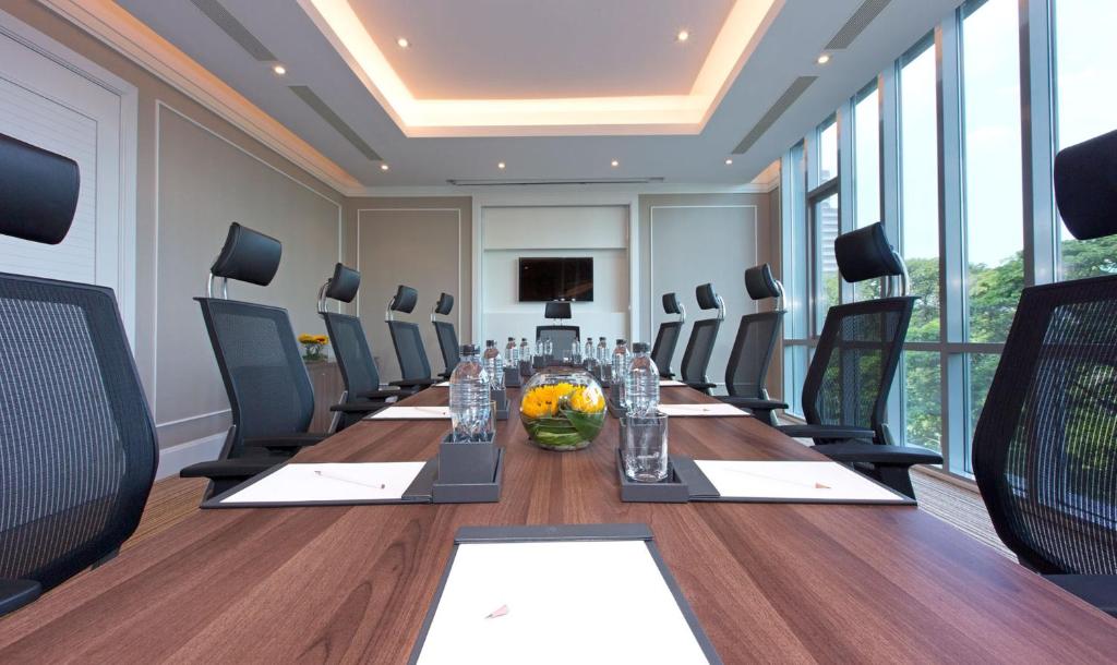 A formal meeting room with a long table, conference chairs, and city-facing windows.