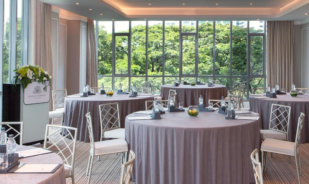 A brightly lit event dining room with dressed round tables and a leafy outlook.