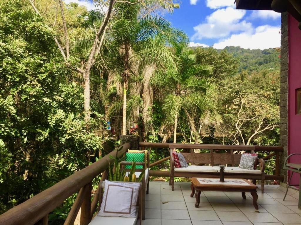 balcón con mesa, sillas y árboles en Villa Cachoeira da Rocha, en Ilhabela