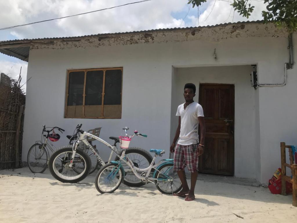 Un uomo in piedi di fronte a una casa con una bicicletta di Moringe Home Stay - Village House a Jambiani