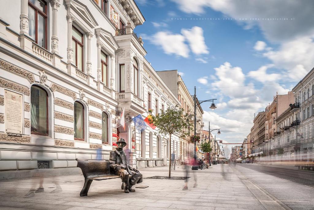 un hombre sentado en un banco en una calle de la ciudad en Royal Aparthotel Piotrkowska 116, en Łódź